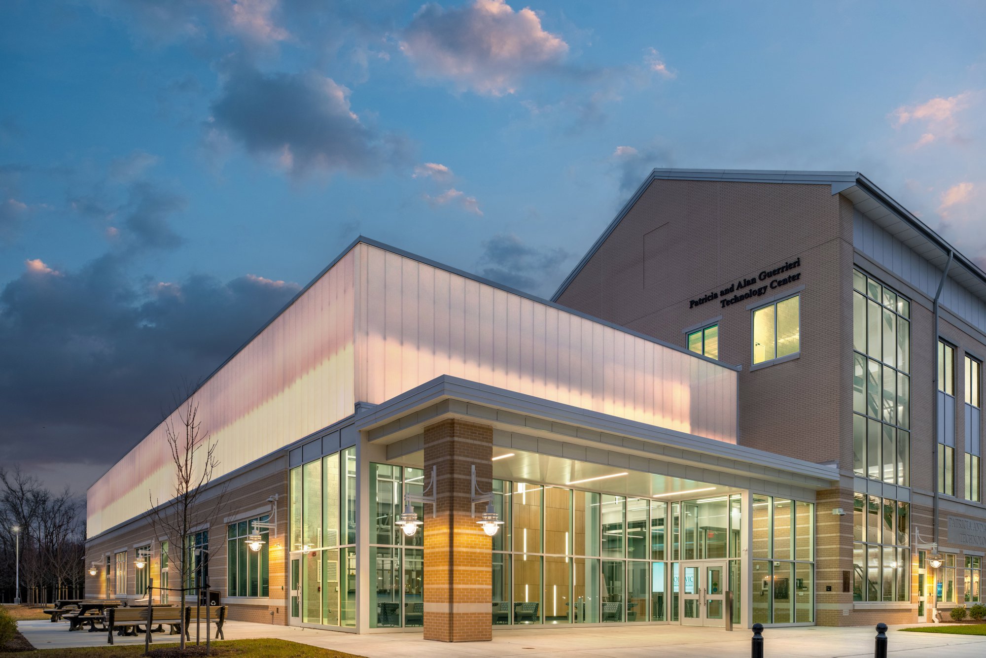 The Patricia and Alan Guerrieri Technology Center at dusk, featuring a modern glass and brick exterior with a glowingly lit, translucent upper facade under a cloudy sunset sky.